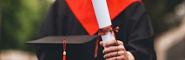 A graduate student in graduation robe holding scroll and cap